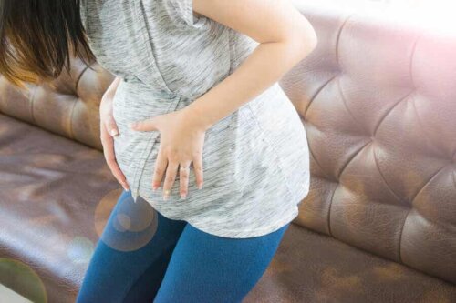Schwangerschaft - Frau setzt sich auf ein Sofa