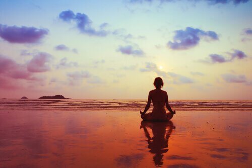 Frau meditiert am Meer im Abendrot und möchte Angst und Nervosität lindern