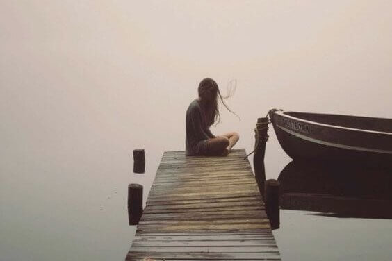 Ein Mädchen sitzt in Stille auf einem Steg am Wasser mit einem Boot.