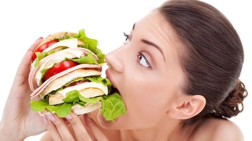 Eine Frau beißt mit Heißhunger in einen Burger, was ein Frühwarnzeichen für Diabetes sein könnte.