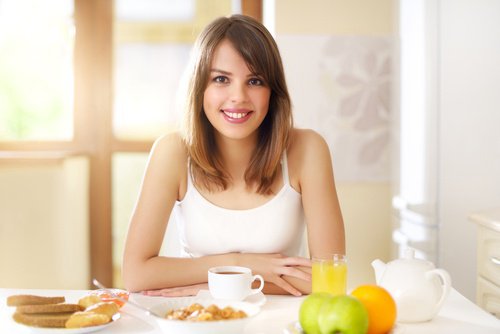 Eine Frau sitzt am Tisch und freut sich auf ein gesundes Frühstück.