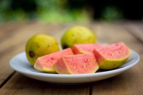 Auf einem Teller liegt eine aufgeschnittene Guave und zwei weitere ganze Guave Früchte.
