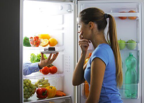 Frau vor dem Kühlschrank isst abends zu viel
