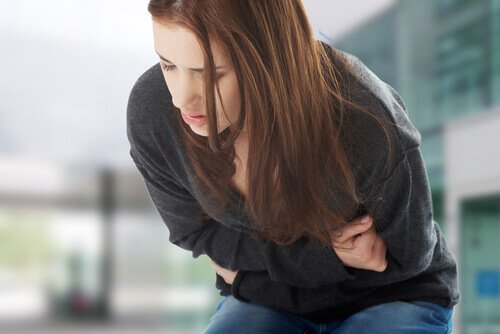 Eine Frau mit Magenschmerzen ist nach vorne gebeugt und hält ihren Bauch mit beiden Händen.