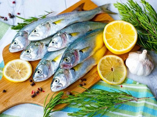 Sieben Fische, voller gesunder Fette, liegen auf einem Holzbrett, umringt von Zitronenschalen.