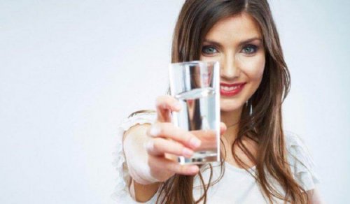 Eine Frau hält ein Glas Wasser vor sich.