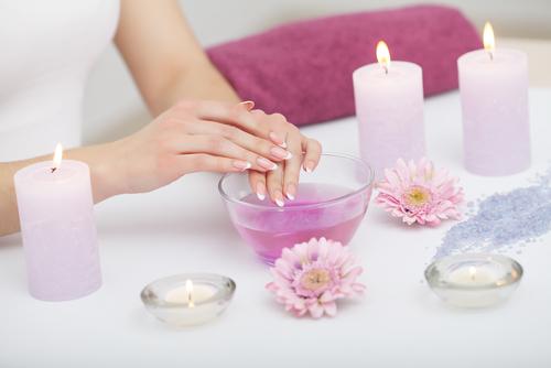 Feuchtigkeitsspendende Flüssigkeit in einer Schüssel, daneben stehen Blumen und Kerzen, während eine Frau ihre Hände am Rand der Schüssel stützt.