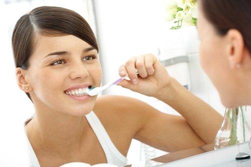 Verhindere schlechten Atem: Eine Frau schaut in den Spiegel, während sie sich die Zähne putzt.