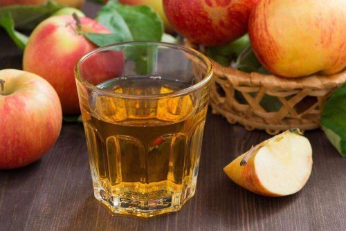 Ein Getränk aus Apfelessig, das gegen starke Menstruationblutungen hilft, steht vor einigen Äpfeln auf einem Tisch.