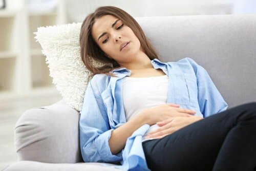 Eine Frau mit Eierstockschmerzen sitzt mit schmerzverzerrtem Gesicht auf der Couch.