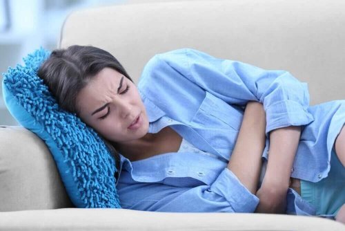 Eine Frau mit Eierstockschmerzen liegt mit schmerzverzerrtem Gesicht auf einer Couch.