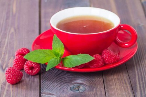 Eine Tasse Himbeertee, neben der einige Himbeeren und Himbeerblätter liegen.