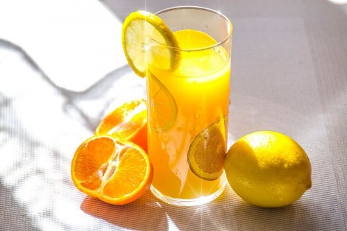 Ein Glas Zitronensaft, neben welchem Zitronen und Orangen liegen.
