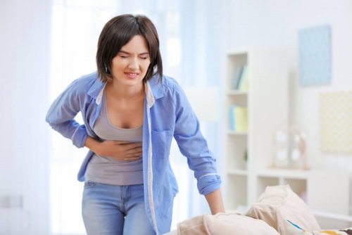 Eine Frau hält sich den Bauch fest, während sie sich an ihre Couch lehnt.