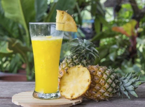 Ein Ananassaft und daben zwei ganze Ananas.