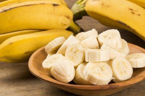 Eine Schale mit aufgeschnittener Banane und dahinter einige ganze Bananen.