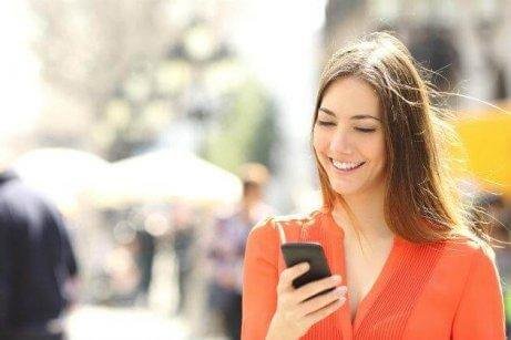 Eine Frau schaut aufs Handy und geht am Gehsteig.