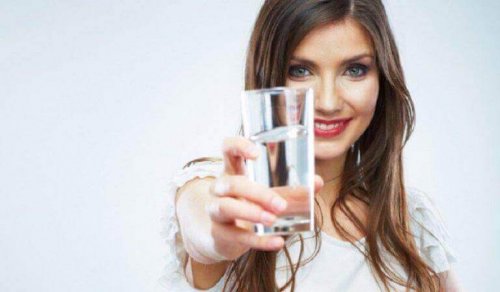 Eine Frau hält ein Glas Wasser mit ausgestreckter Hand.