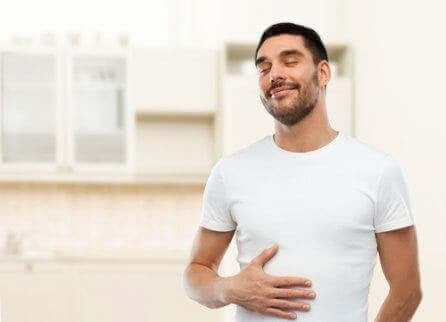 Ein Mann hält sich lächelnd den Bauch, da ihm Wermut bei der Verdauung geholfen hat.