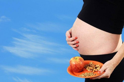 Eine schwangere Frau hält einen Teller mit Lebensmitteln.