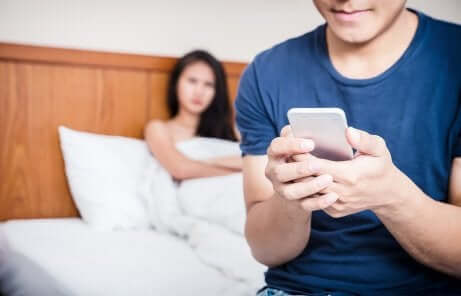 Paarbeziehung: Frau sieht vom Bett aus auf ihren Partner mit Handy