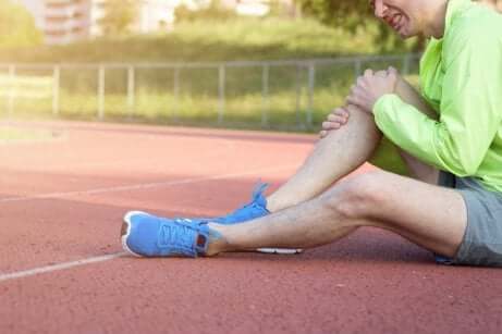Sportler sitzt auf Aschenbahn und hält sein Knie