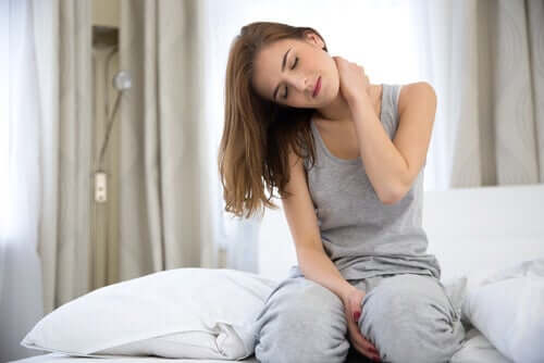 Frau mit Nackenschmerzen sitzt auf dem Bett