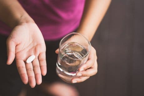 Person mit Paracetamol und einem Glas Wasser in der Hand