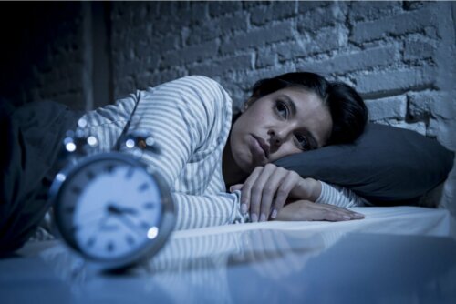 Frau im Bett schaut auf Uhr schlaflos