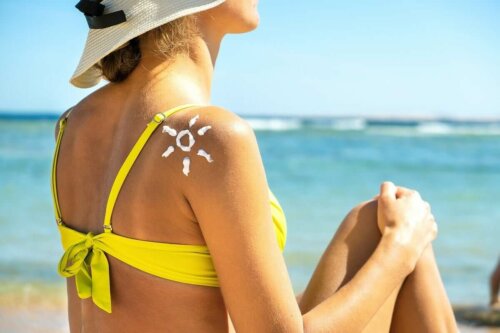 Eine Frau sitzt am Strand mit einer Sonne aus Sonnencreme auf der Schulter